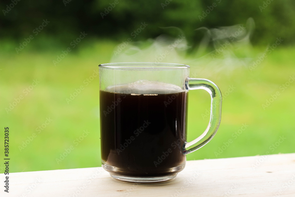 A glass transparent cup with black coffee, from which steam is rising. A glass transparent cup with black coffee, from which steam is rising.