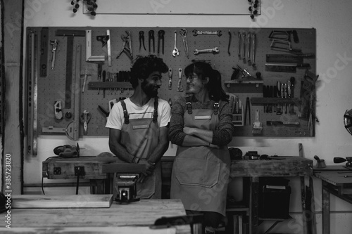 Young couple of carpenters having a break in their home made carpentry workshop together with a dog. Team of wood worker relaxing in front of the tool board panel for the lunch break. Family business