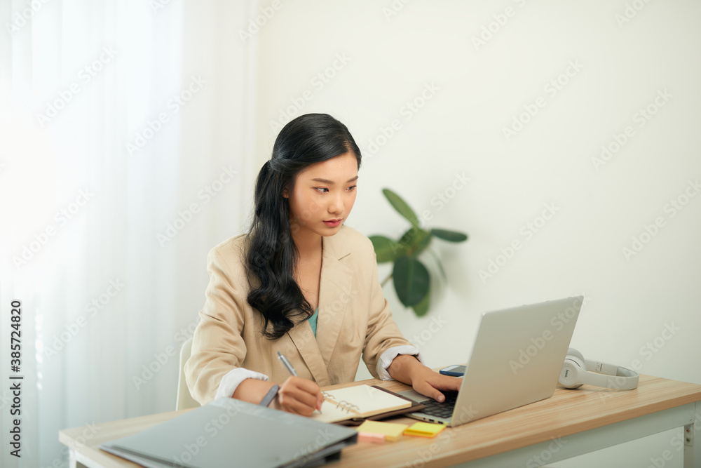 Beautiful young woman in casual clothing using laptop and smiling while working indoors Beautiful young woman in casual clothing using laptop and smiling while working indoors