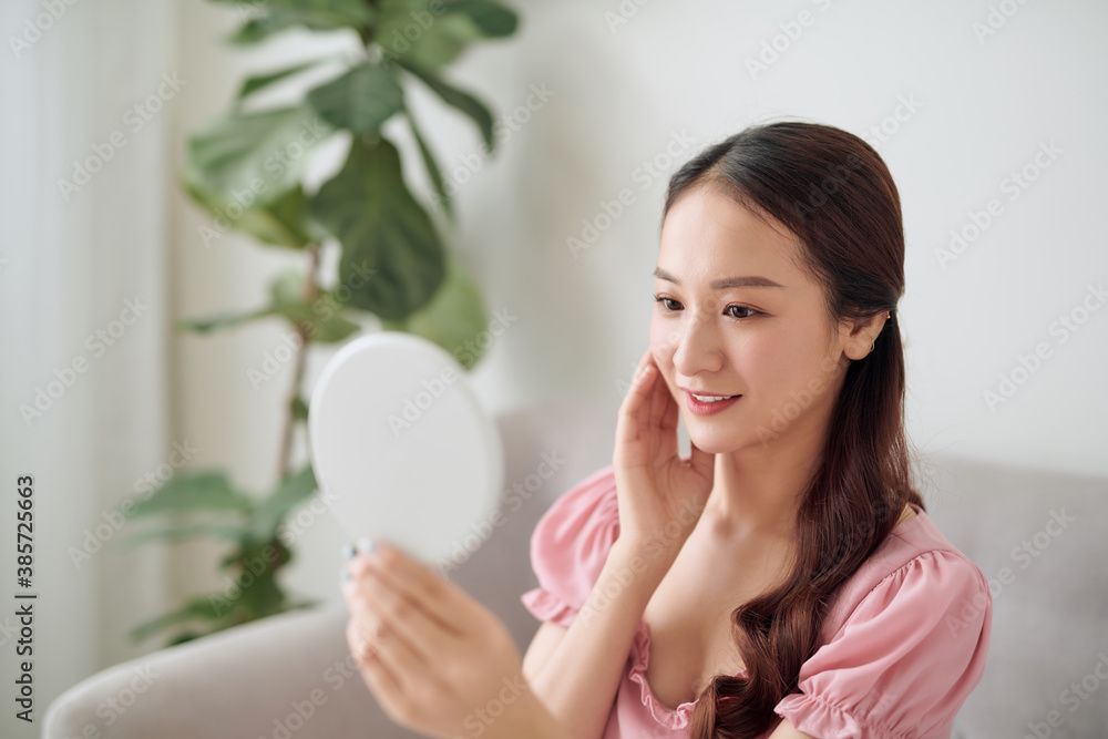 Beautiful young woman looking in the mirror while sitting in the sofa Beautiful young woman looking in the mirror while sitting in the sofa