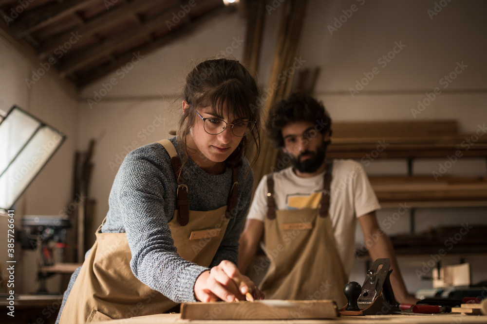 Young couple of carpenter working and crafting with wood in a workshop building furniture for interior design. Young couple entrepreneurs running a small business in a carpentry. Business people.