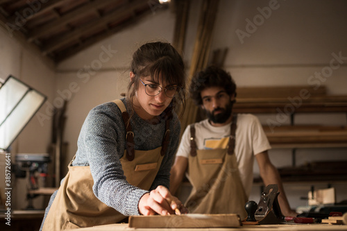 Obraz na płótnie Young couple of carpenter working and crafting with wood in a workshop building furniture for interior design. Young couple entrepreneurs running a small business in a carpentry. Business people. w salonie