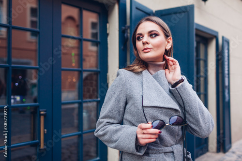 Beauty portrait of stylish woman walking on city street. Autumn fashion female accessories and clothes.