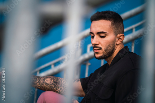 Chico joven tatuado en escaleras metálicas junto a edificio azul