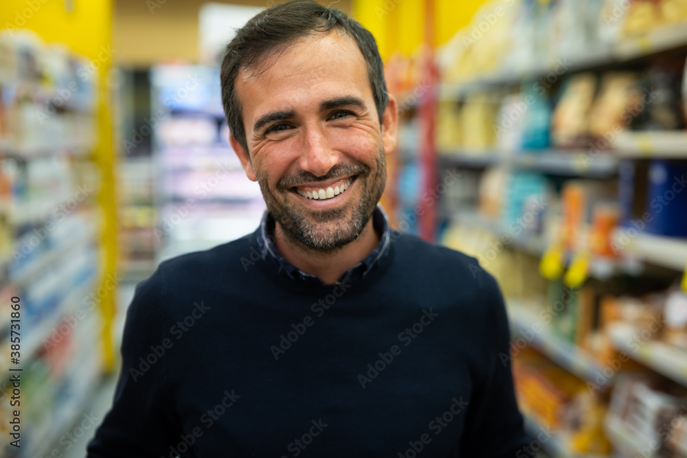 Authentic close up shot of happy young man is smiling in camera with shopping cart with chosen food products while going for groceries in supermarket. Authentic close up shot of happy young man is smiling in camera with shopping cart with chosen food products while going for groceries in supermarket.