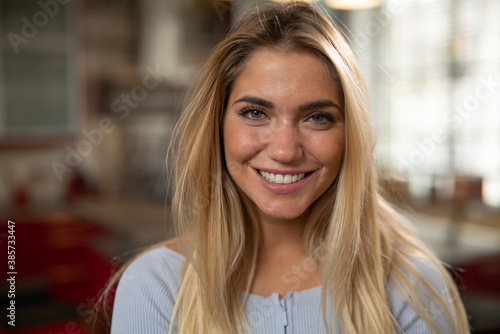 Authentic close up shot of an young blond hair attractive happy woman is smiling in camera in a living room at home.