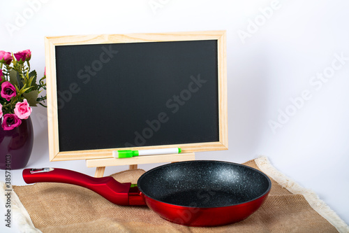 Empty black-red frying pan on linen table cloth and mini easel. It`s blank for copy, text or your words or sent. Folded tablecloth and frying pan photo