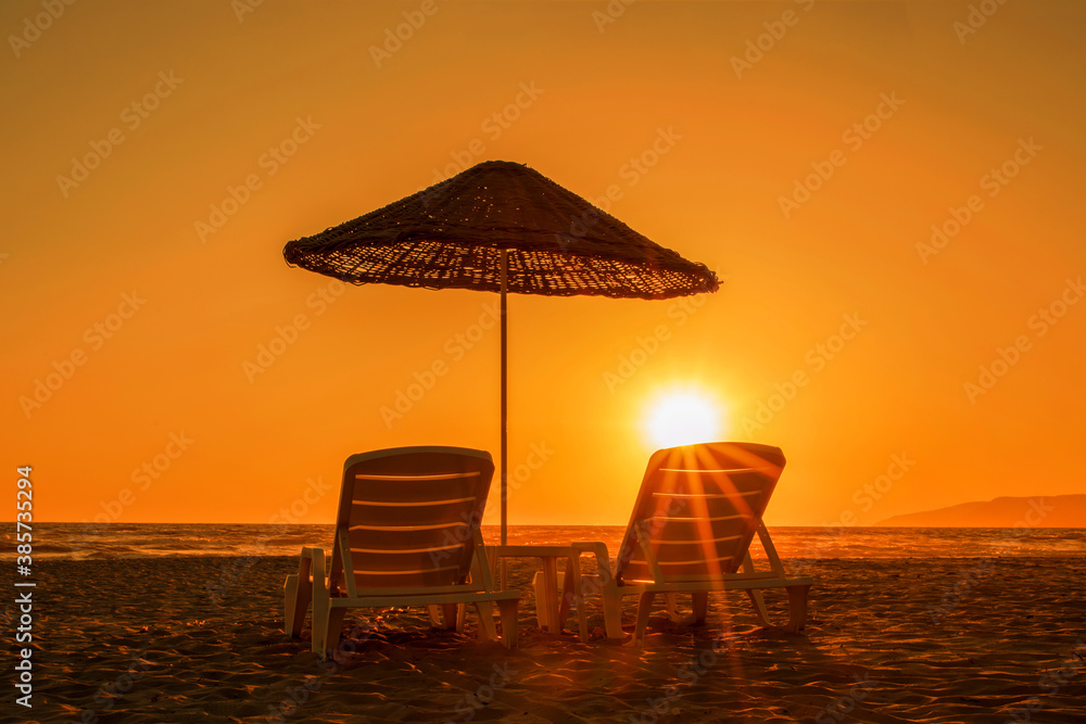 two sunbeds under big umbrella on sandy beach in sunset time
