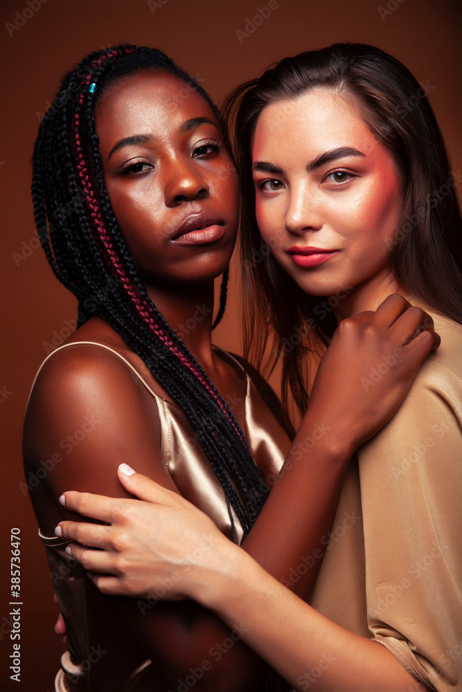 young pretty caucasian, afro woman posing cheerful together on brown background, lifestyle diverse nationality people concept young pretty caucasian, afro woman posing cheerful together on brown background, lifestyle diverse nationality people concept