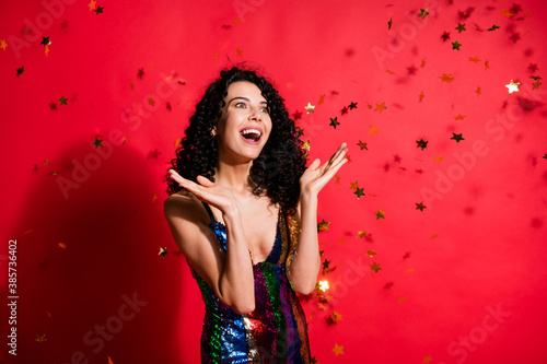 Photo of amazed young girl open mouth look empty space golden stars fall wear glossy mini dress isolated vivid red color background