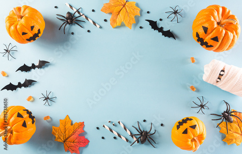 Halloween decorations made from pumpkin, paper bats and black spider on pastel blue background. Flat lay, top view with copy space for text.