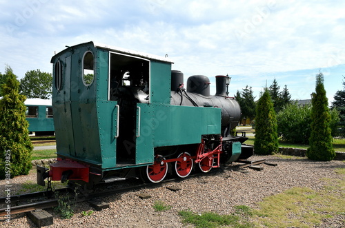 Close up on a vintage train with a green metal body and red and white wheels standing on a side track surrounded with some trees and with a single carriage visible in the background in Poland
