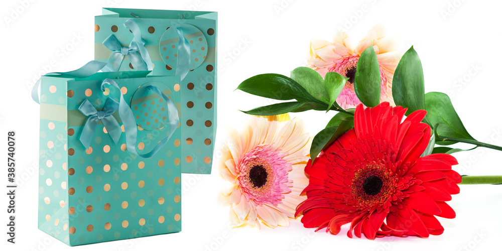Obraz premium Turquoise paper bag with satin ribbon handles for gift wrapping with a bouquet of gerbera flowers, isolated on a white background,copy space