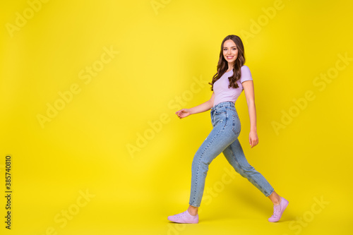 Fototapeta Naklejka Na Ścianę i Meble -  Full length body size profile side view of lovely cheerful wavy-haired girl walking copy space isolated over bright yellow color background
