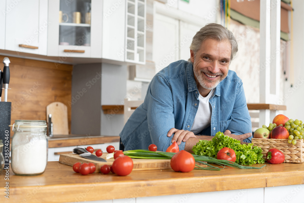 Grey-haired Mature handsome caucasian man standing in the bright kitchen. Grey-haired Mature handsome caucasian man standing in the bright kitchen.