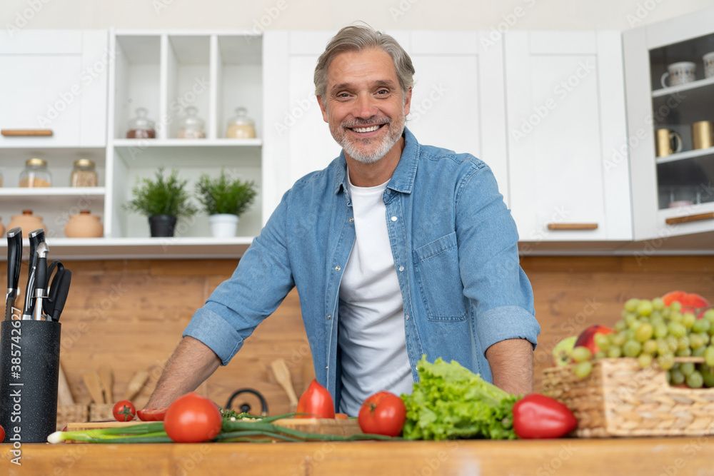 Fototapeta premium Grey-haired Mature handsome caucasian man standing in the bright kitchen.