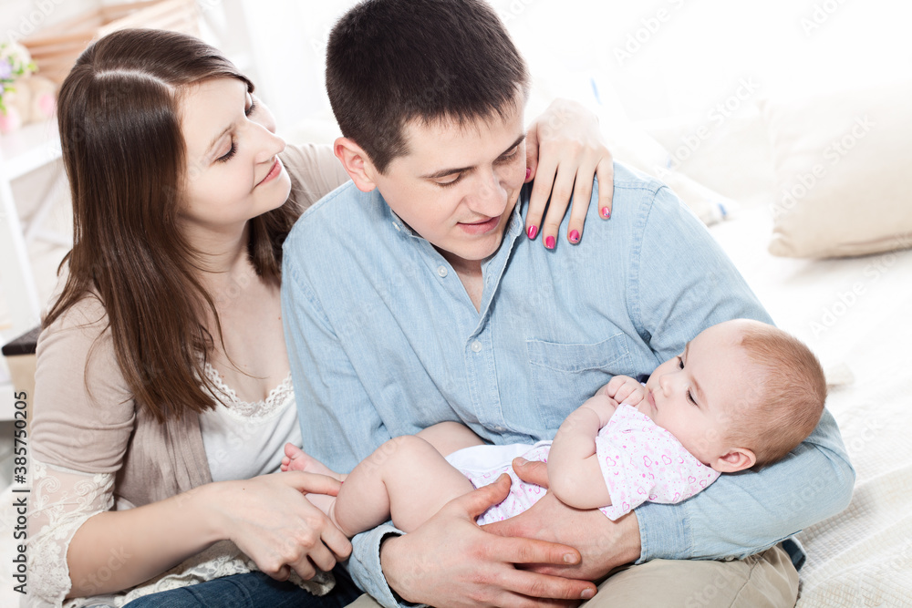 Portrait of happy young parents with baby in the bed at home