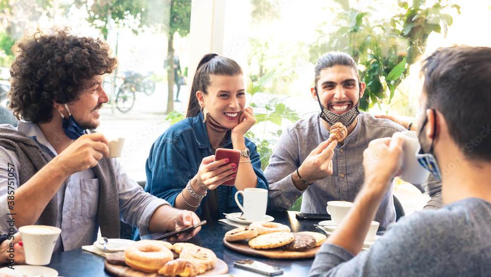 happy group of friends smiling at breakfast into a cafe whilst interacting with technology. mates drinking coffee and eating. concept about friendship and new normality