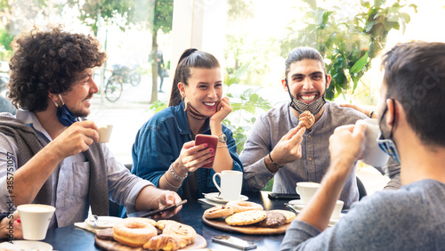 happy group of friends smiling at breakfast into a cafe whilst interacting with technology. mates drinking coffee and eating. concept about friendship and new normality photo