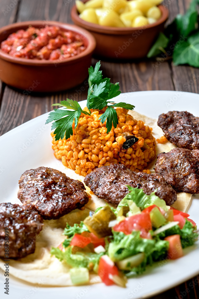 Kofte (köfte) - Turkish cutlets (meat balls) made from lamb and beef meat and spices, cooked over charcoal. Served on a platter with salad and bulgur. Close-up Kofte (köfte) - Turkish cutlets (meat balls) made from lamb and beef meat and spices, cooked over charcoal. Served on a platter with salad and bulgur. Close-up