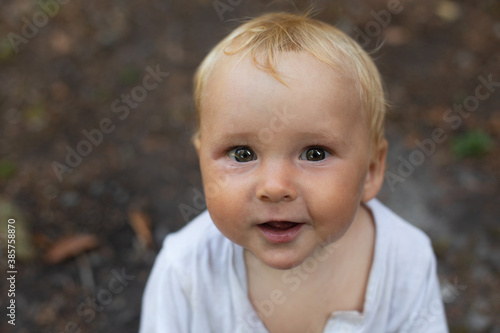 Portrait of cheerful blond baby boy having fun outside. Boy is looking at camera. Background is natural in calm colors