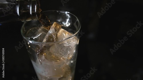 dark soda is poured into a glass with ice close-up