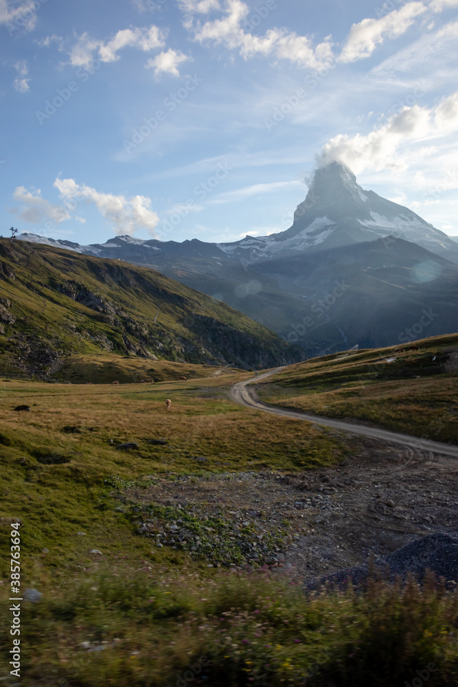 Road in the grass with the Matterhorn in the background on a summer evening in the Valais Alps of Switzerland. 