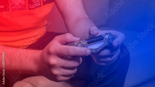Male hands with game joystick, gamepad. Close-up. The young guy is playing the console. Red blue neon light.