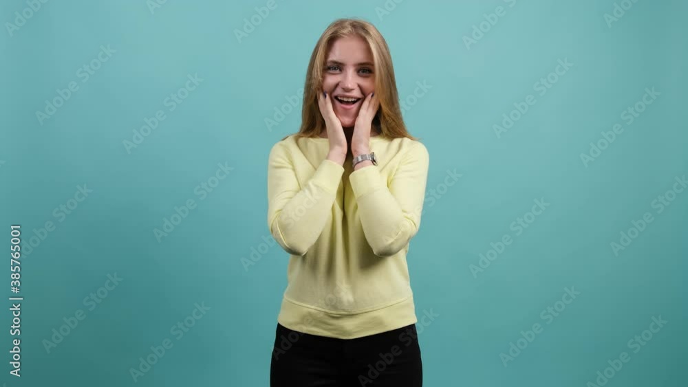 Young woman puts her hand to her face over turquoise background. Surprised caucasian girl. Young woman puts her hand to her face over turquoise background. Surprised caucasian girl.