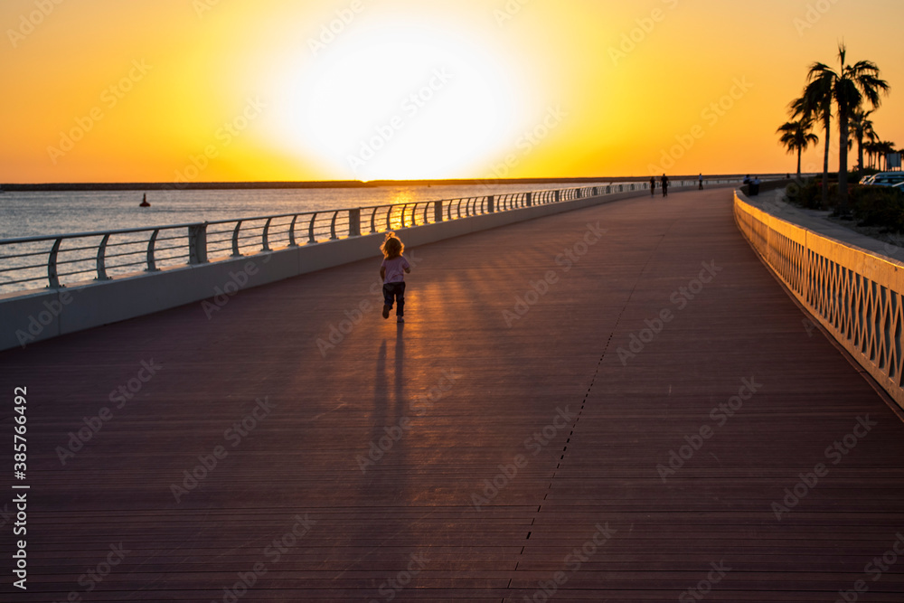 Little girl running on the boardwalk during sunset hour.
