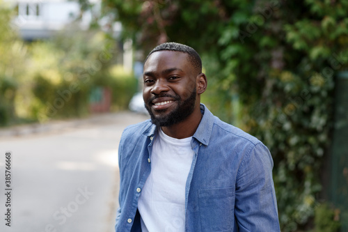 Close up portrait of a happy African American man. Handsome young man in blue denim shirt walking in the street and smiling.