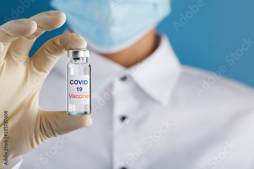 An ampoule with the inscription COVID-19 vaccine in the hands of a doctor-scientist in rubber gloves with a vaccine.