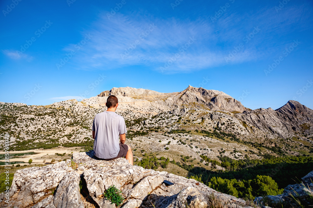 Man at the top of a mountain looking the landscape, Young man sitting on rock, Majorca mountains