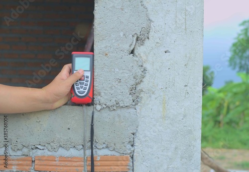 Red laser meter, digital ultrasonic distance measuring device, handheld device, window frame, window openings under construction, brick wall, concrete wall background, concrete column corner, 