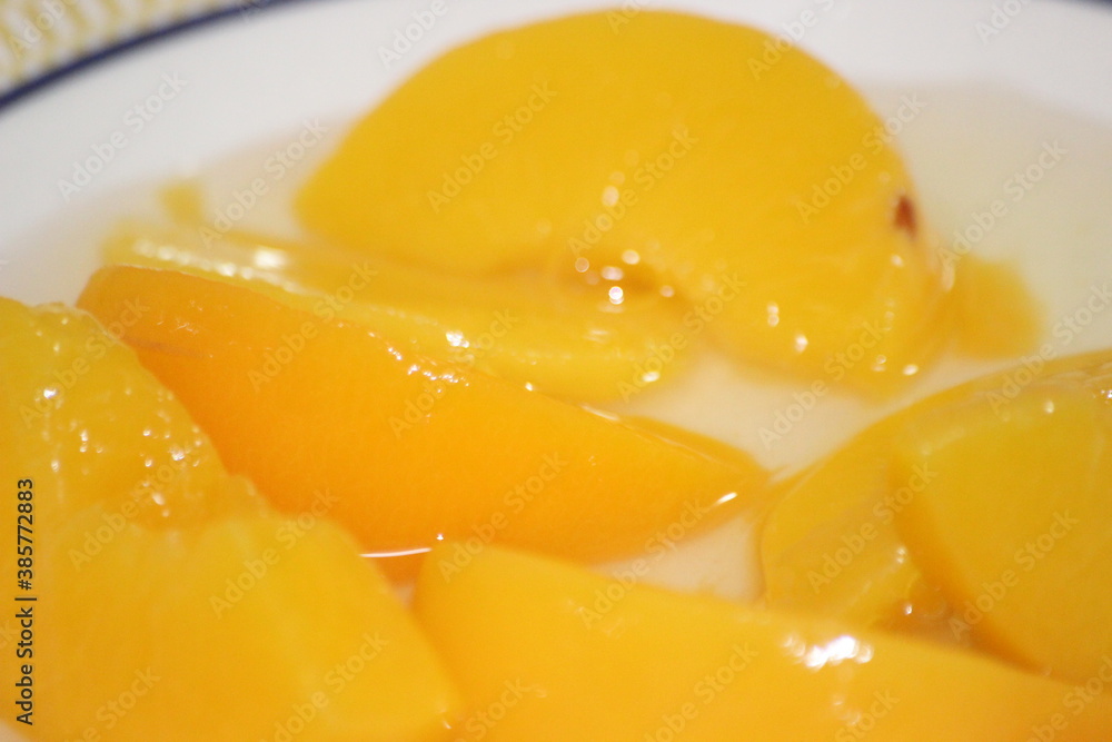 Canned peaches halves sprinkled with syrup in white plate.