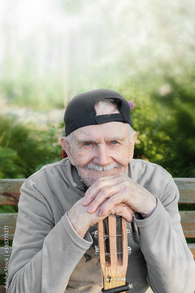old mustachioed male rocker sits with an acoustic guitar outdoors in ...