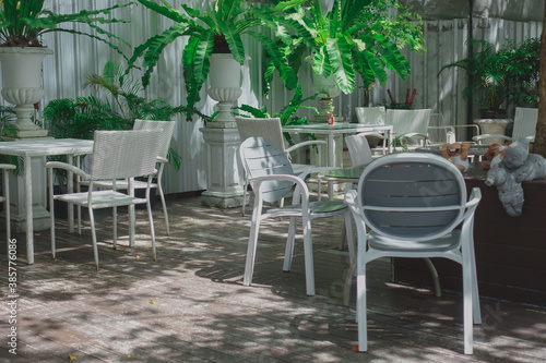 A white Metal outdoor garden furniture, table and chair set in the home small garden under the tree shade with the afternoon light.