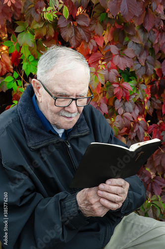 Healthy looking old man is his late 87s sitting in garden at home and reading book photo