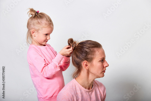 4-5 year old little daughter does the hair of a her mother. Love family spending time together in pink clothes