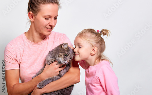 Happy mother with her daughter is holding cat on gray background