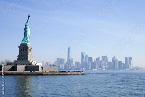 Statue of Liberty in NY Harbor on bright sunny day with blue sky and Manhattan in the distance