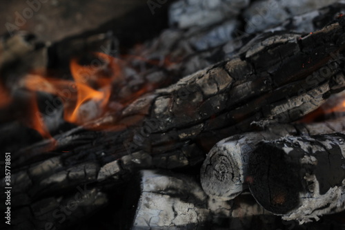 Smoldered logs burned in vivid fire close up. Atmospheric background with flame of campfire. Unimaginable detailed image of bonfire from inside with copy space. Whirlwind of smoke and glowing embers.