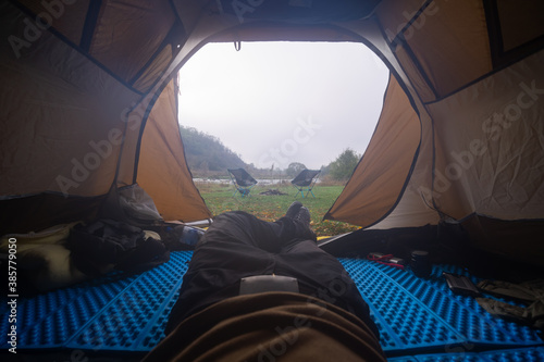 Inside the tourist tent, first person view. Foggy morning near the river. Folding chair and table. Tourism and hobby. Man legs