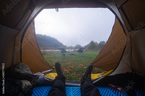 Inside the tourist tent, first person view. Foggy morning near the river. Folding chair and table. Tourism and hobby. Man legs