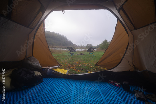Inside the tourist tent, first person view. Foggy morning near the river. Folding chair and table. Tourism and hobby.
