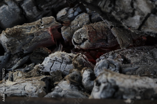 Smoldered logs burned in vivid fire close up. Atmospheric background with flame of campfire. Unimaginable detailed image of bonfire from inside with copy space. Whirlwind of smoke and glowing embers.