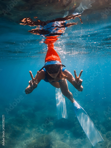 Happy freediver woman with New year cap glides underwater in blue sea. Christmas holidays concept