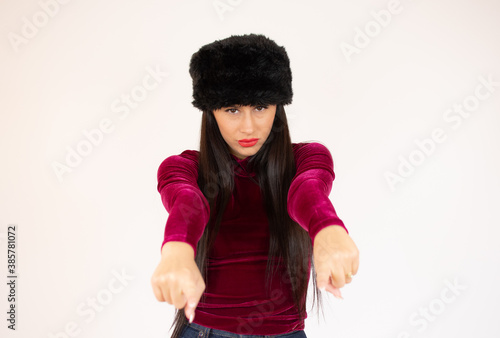 Young woman in winter clothes over isolated white wall points finger at you.