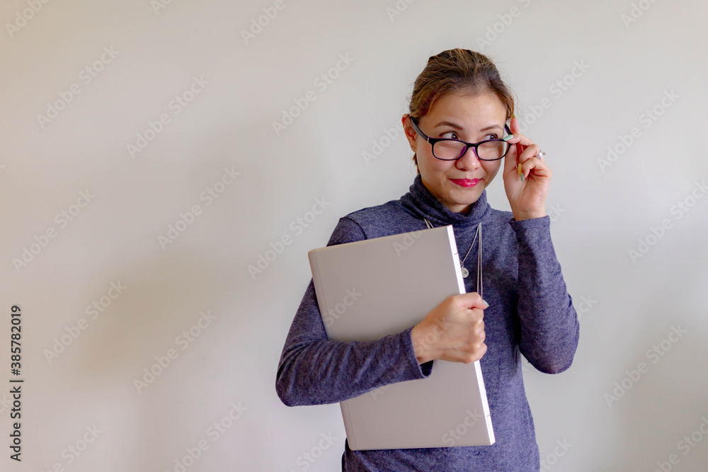 One successful and happy young adult business woman holding a laptop with smile. Professional female worker standing in corporate modern office and window in casual gray look. - With copy space. One successful and happy young adult business woman holding a laptop with smile. Professional female worker standing in corporate modern office and window in casual gray look. - With copy space.