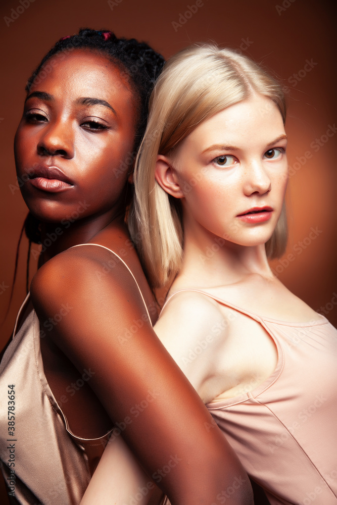 two pretty girls african and caucasian blond posing cheerful together on brown background, ethnicity diverse lifestyle people concept two pretty girls african and caucasian blond posing cheerful together on brown background, ethnicity diverse lifestyle people concept